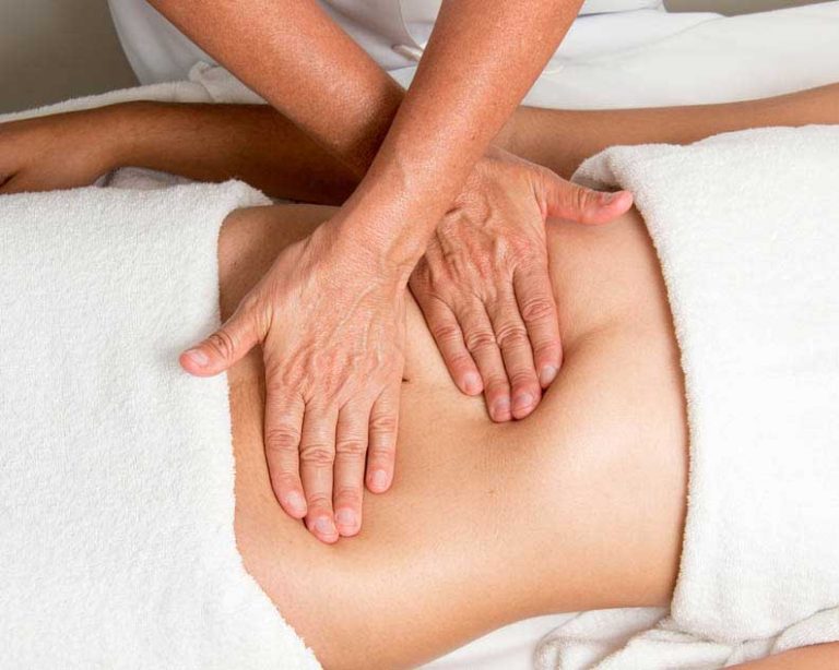 Close up of masseuse's hands putting gentle pressure on woman's stomach, draped in white towels.